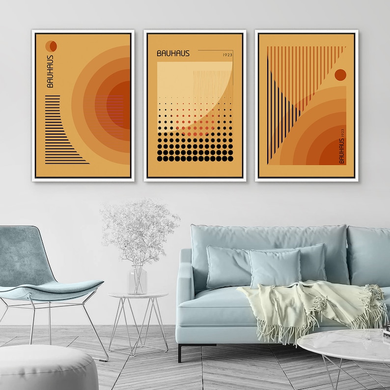 May include: A set of three rectangular wall art prints featuring Bauhaus-inspired geometric designs in shades of orange, yellow, and black. Each print displays abstract patterns, including concentric circles, dots, and vertical lines with the text Bauhaus 1923.
