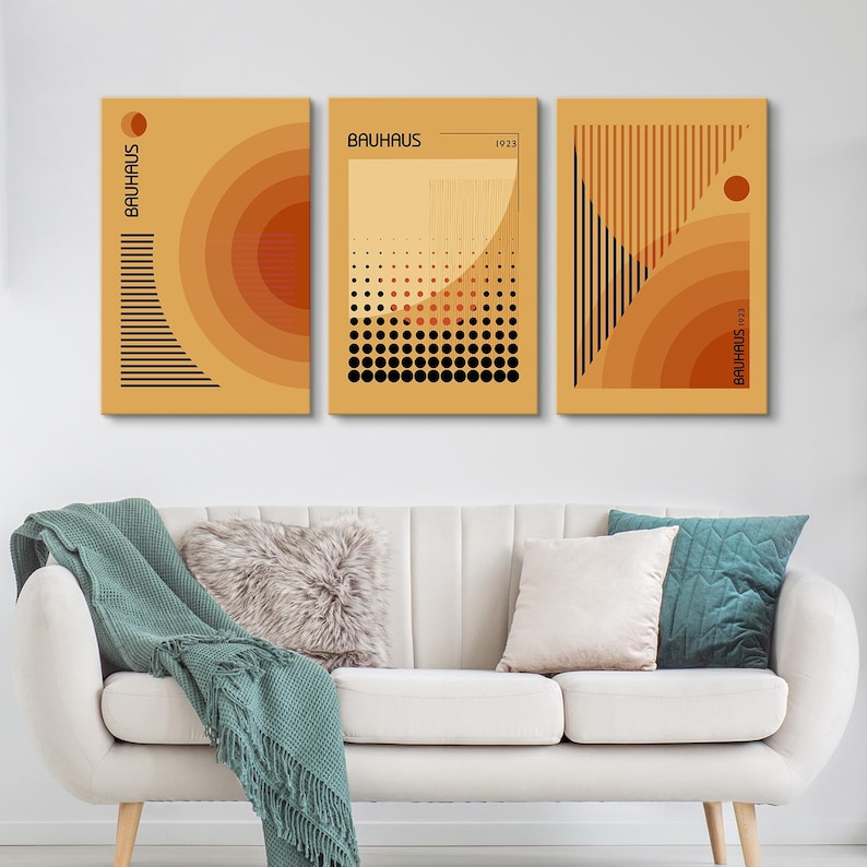 May include: A set of three rectangular wall art prints featuring Bauhaus-inspired geometric designs in shades of orange, yellow, and black. The prints display concentric circles, vertical lines, dot patterns, and the text Bauhaus 1923.