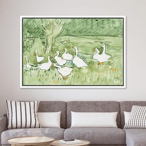 May include: Watercolor painting of a flock of white geese in a green field with yellow flowers. The artwork is framed in a white border and hangs above a gray sofa. The background features a tree and a light green wash.