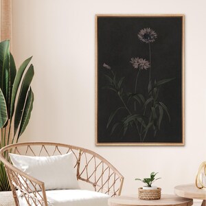 Puede incluir: Una impresi&oacute;n bot&aacute;nica enmarcada con un fondo oscuro, que presenta una ilustraci&oacute;n detallada de flores y hojas en tonos grises y morados. La obra de arte est&aacute; enmarcada en un marco de madera marr&oacute;n claro, a&ntilde;adiendo un toque de elegancia natural.