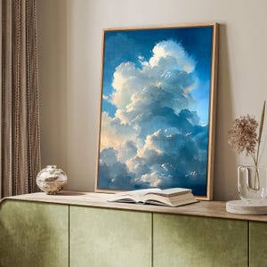 May include: A framed art print depicting a dramatic cloudscape with shades of blue, white, and gold. The artwork is displayed on a light-colored wooden frame. A book is open in front of the artwork, and a decorative vase is to the side.