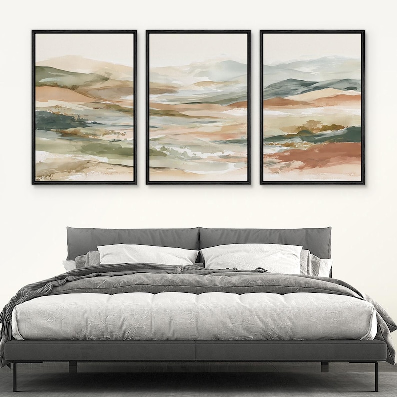 May include: Three framed abstract landscape paintings. Each features a watercolor style with muted tones of green, beige, and rust. The artwork is displayed above a gray bed frame with white bedding.
