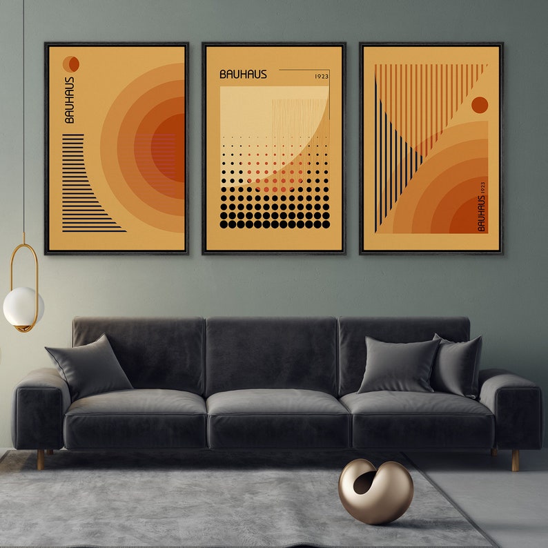May include: A set of three framed wall art prints featuring geometric Bauhaus designs in shades of orange, yellow, and black. Each print displays abstract patterns, including concentric circles, dots, and vertical lines, with the text BAUHAUS 1923.