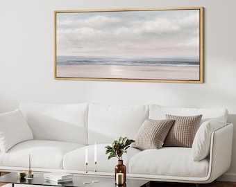 May include: A framed landscape painting depicts a serene beach scene. The artwork features a light blue sky with fluffy clouds, a calm ocean, and a sandy beach. The frame is a light wood color.