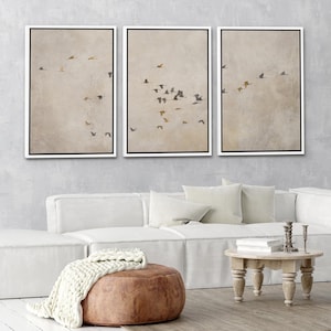 May include: Three framed prints of a minimalist abstract art design featuring a flock of birds flying in a beige sky. The prints are in black frames with white mats.