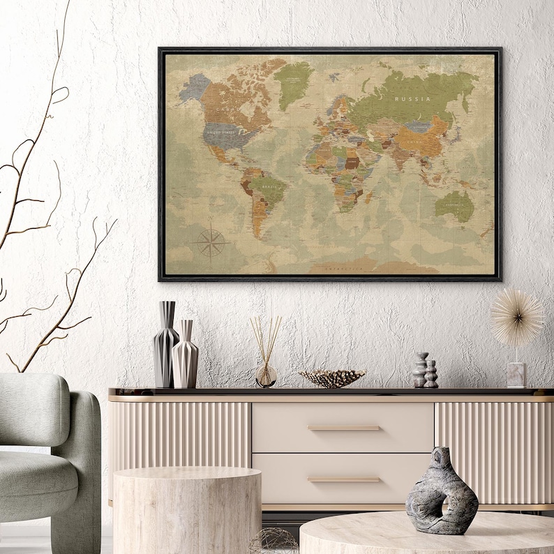 Puede incluir: Un mapa del mundo enmarcado con una est&eacute;tica vintage. El mapa presenta una paleta de colores apagados de verdes, marrones y azules, con las fronteras y los nombres de los pa&iacute;ses claramente marcados. El marco es negro y el mapa se muestra encima de un mueble moderno.