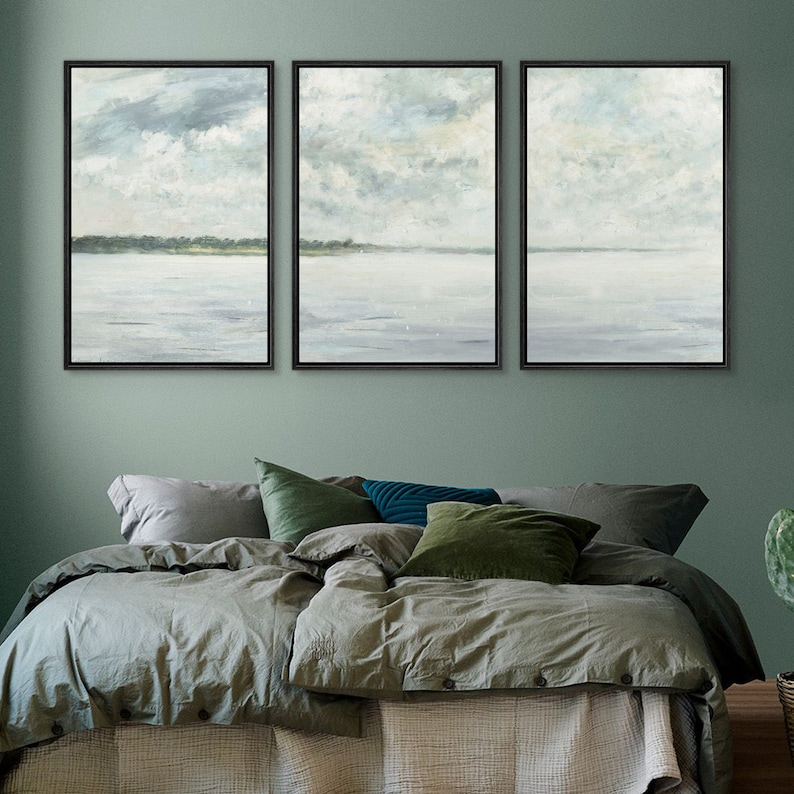 May include: Three framed landscape paintings with a muted color palette of light blues and grays. The paintings depict a seascape with a distant shoreline and cloudy sky.