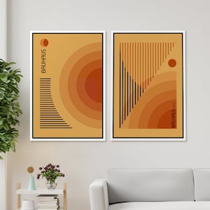 May include: Two framed rectangular wall art prints featuring abstract geometric designs in shades of orange, yellow, and black. The left print displays concentric circles and horizontal lines with the text BAUHAUS. The right print shows vertical lines and circles with the text BAUHAUS 1923.