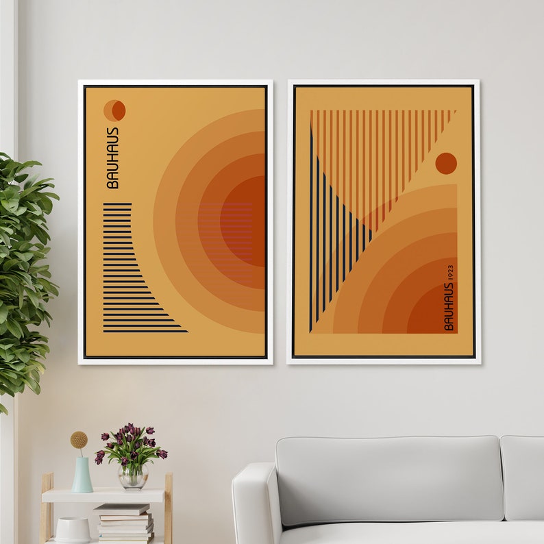 May include: Two framed rectangular wall art prints featuring abstract geometric designs in shades of orange, yellow, and black. The left print displays concentric circles and horizontal lines with the text BAUHAUS. The right print shows vertical lines and circles with the text BAUHAUS 1923.