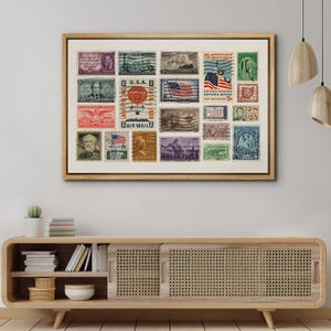 May include: A framed collection of vintage U.S. postage stamps. The stamps feature various designs, including portraits, flags, and historical scenes. The frame is a light brown color and is displayed on a wooden cabinet.