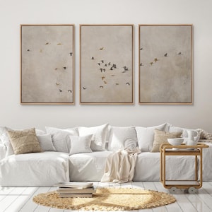 May include: Three framed canvas prints with a beige background and a flock of birds flying in a V formation. The birds are painted in shades of brown, gray, and gold.