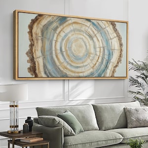May include: A rectangular wall art piece featuring a cross-section of a tree trunk with concentric rings in shades of beige, brown, and soft blue. The artwork is enclosed in a light-colored wooden frame, displaying a textured, organic pattern.