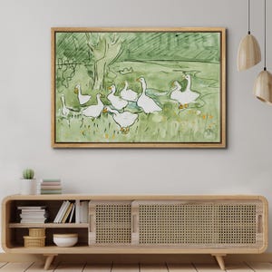 May include: Watercolor painting of a flock of white geese in a green field with a tree in the background. The artwork is framed in a light brown wooden frame. The style is simple and illustrative.