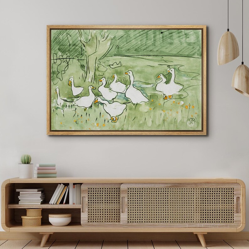 May include: Watercolor painting of a flock of white geese in a green field with a tree in the background. The artwork is framed in a light brown wooden frame. The style is simple and illustrative.