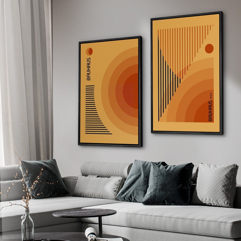 May include: Two framed wall art prints featuring abstract geometric designs in shades of yellow and orange. The left print displays concentric circles and horizontal lines with the text BAUHAUS. The right print shows vertical lines and the text BAUHAUS 1923.