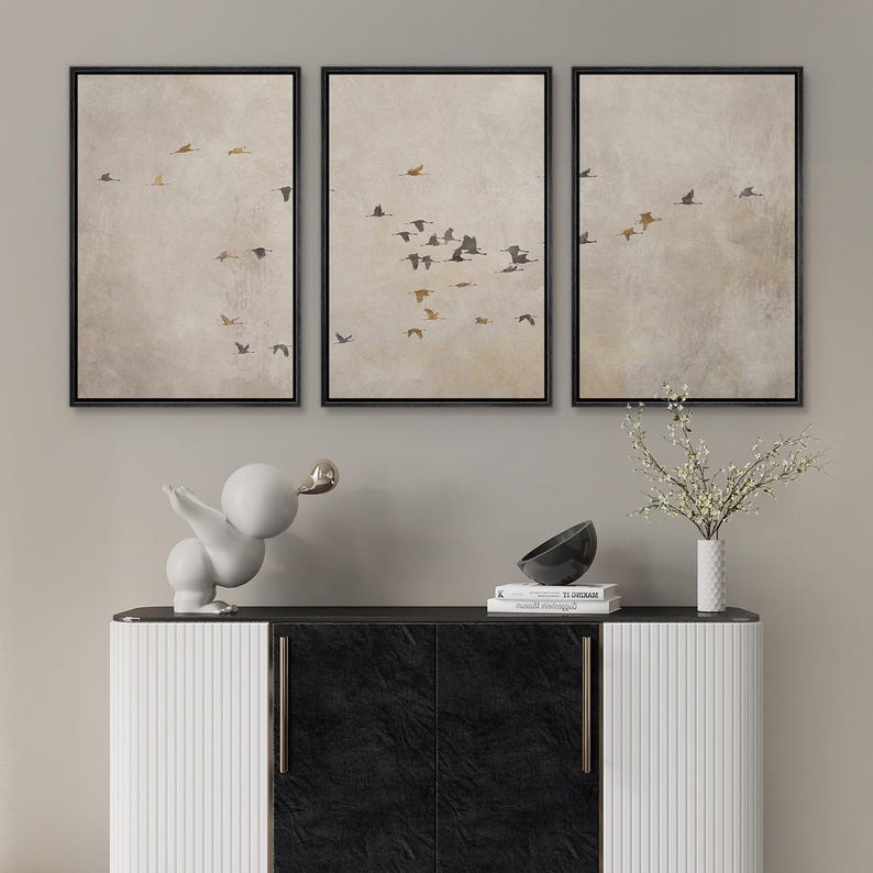 May include: Three framed prints of a flock of birds flying in formation against a light beige background. The prints are arranged in a row on a wall above a white and black cabinet.