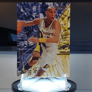 May include: A basketball trading card featuring a player in a yellow and blue jersey with the word "Bucks" on the front. The card has a silver foil background with a holographic effect.
