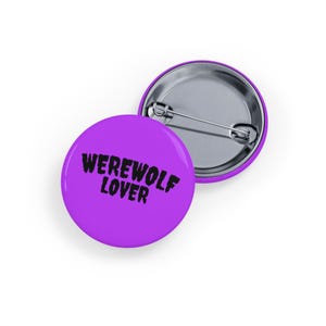 Puede incluir: Dos insignias redondas moradas con la frase "WEREWOLF LOVER" en negro. El texto está impreso en negrita en la parte delantera. La parte trasera de las insignias es de metal plateado con cierre de imperdible.