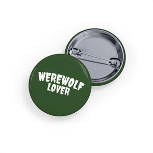 Puede incluir: Dos insignias redondas verdes de "Werewolf Lover". Una muestra el texto blanco "WEREWOLF LOVER". La otra muestra el alfiler. Las insignias están sobre un fondo blanco.