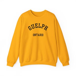 May include: Mustard yellow sweatshirt featuring the word "GUELPH" in black, arched lettering, with "ONTARIO" printed underneath. The crew neck sweatshirt has long sleeves.