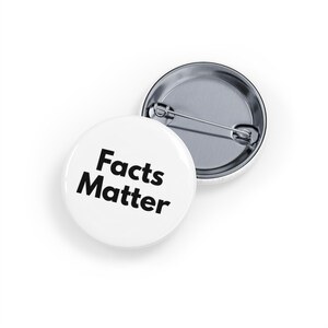 Può includere: Una spilla rotonda con superficie bianca e il testo nero "Facts Matter" stampato in un carattere sans-serif in grassetto. Il retro della spilla è in metallo argentato e presenta un meccanismo a spilla orizzontale per l'attacco ai vestiti.