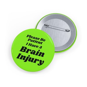 May include: A round pinback button with a bright lime green front featuring the black text "Please Be Patient I Have A Brain Injury" in a bold serif font. The back of the button is metallic silver with a horizontal metal pin mechanism attached.