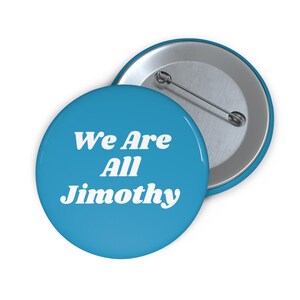 Op de afbeelding: Een ronde button met een helderblauwe achtergrond en witte tekst die We Are All Jimothy leest. De achterkant van de button is van zilverkleurig metaal en is voorzien van een horizontale speld om aan kleding te bevestigen.