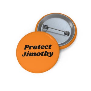 Op de afbeelding: Twee ronde buttons met een speldsluiting en een feloranje oppervlak. Eén button ligt met de voorkant naar boven en toont de zwarte tekst 'Protect Jimothy' in een vetgedrukt schreeflettertype. De andere button toont de zilverkleurige metalen achterkant.