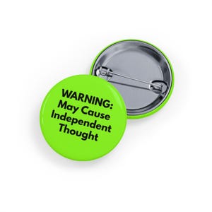 Può includere: Due spille rotonde verde lime. Una spilla mostra il testo "WARNING: May Cause Independent Thought" in nero. La seconda spilla è parzialmente visibile sullo sfondo. Le spille hanno un retro in metallo argentato.