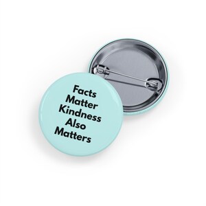 Può includere: Una spilla rotonda con superficie azzurra che riporta il testo nero Facts Matter Kindness Also Matters. Il retro della spilla è in metallo argentato con un meccanismo a spilla orizzontale per il fissaggio su indumenti o tessuti.