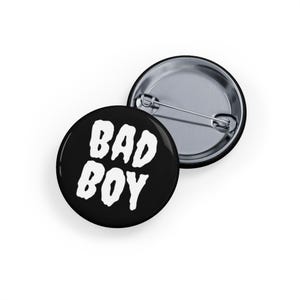 May include: A white ceramic mug with a black handle and the text "But First, Coffee" in a bold, black font. The mug is set against a blurred background. The mug appears to be approximately 10 cm tall.