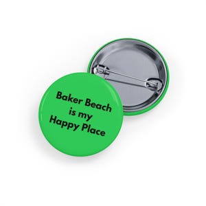 May include: Two green round pin badges. One badge displays the text "Baker Beach is my Happy Place" in black. The other badge is green with a silver pin on the back.