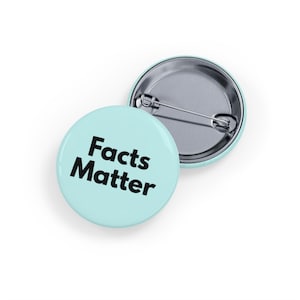 Può includere: Una spilla rotonda con una superficie azzurra e il testo nero "Facts Matter" stampato in un carattere sans-serif in grassetto. Il retro della spilla è in argento metallizzato e presenta un meccanismo a spilla orizzontale per l'attacco.