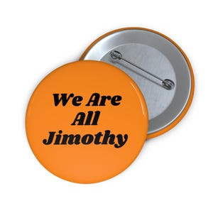 Op de afbeelding: Een ronde oranje button met de zwarte tekst "We Are All Jimothy" in het midden. De achterkant van de button is van zilverkleurig metaal en is voorzien van een horizontale speld voor bevestiging aan kleding of stoffen accessoires.