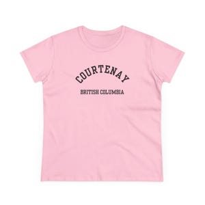 Peut inclure: T-shirt rose clair avec l'inscription "COURTENAY" en noir, arquée en haut, et "BRITISH COLUMBIA" en dessous. Le t-shirt est à col rond et à manches courtes.
