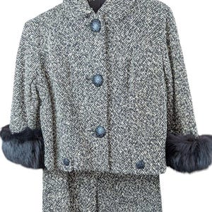 Könnte beinhalten: Ein Vintage-Tweed-Anzug in Grau- und Weißtönen, mit einer kurzen Jacke mit drei dekorativen Knöpfen und Pelzbündchen. Der passende Rock vervollständigt das klassische zweiteilige Ensemble.