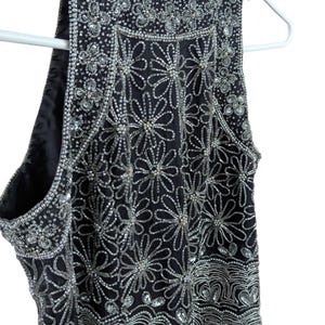 May include: Black sleeveless top with intricate silver bead and sequin floral and wave patterns. The top is embellished with sparkling beads and sequins, creating a glamorous and eye-catching design. The garment is hanging on a white hanger.