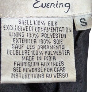 May include: A close-up of a Papell Boutique Evening label. The label is white with black text, including "SHELL: 100% SILK" and "MADE IN INDIA". The size is "S". The background is black.