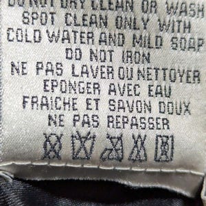 May include: A close-up of a fabric tag with care instructions in English and French. The tag reads "DO NOT DRY CLEAN OR WASH" and "SPOT CLEAN ONLY WITH COLD WATER AND MILD SOAP". It also includes symbols for care.