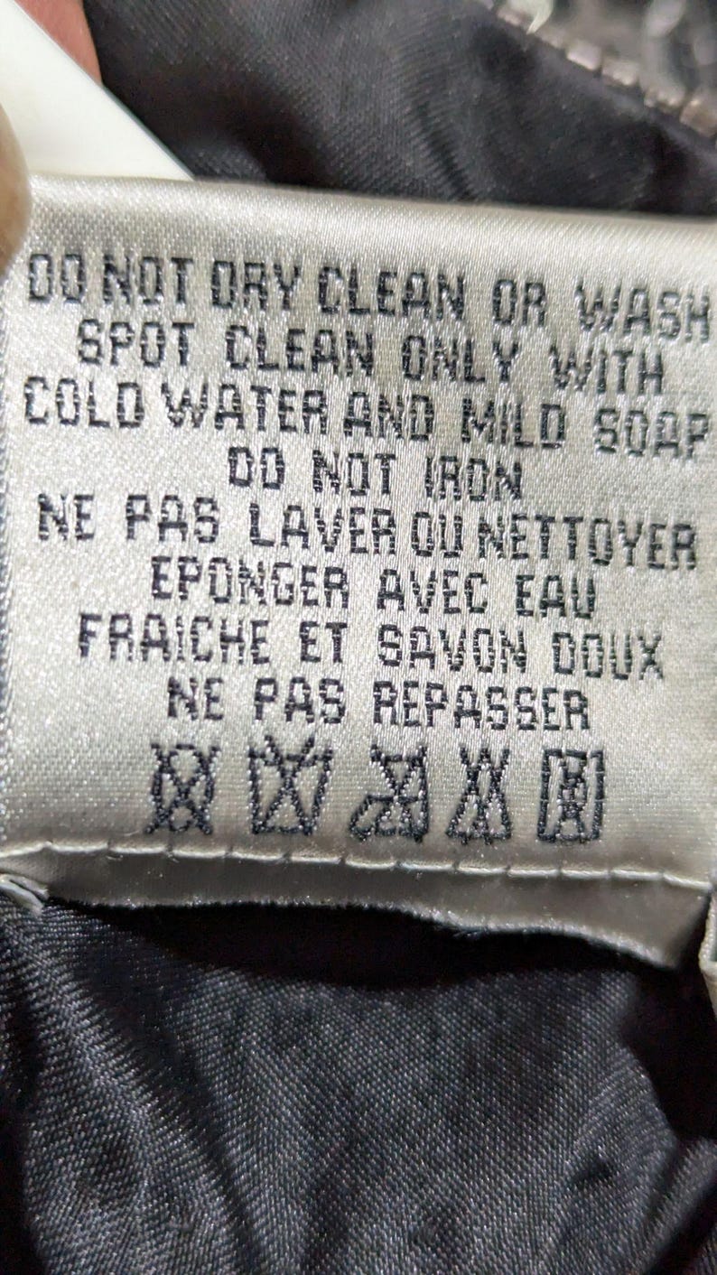 May include: A close-up of a fabric tag with care instructions in English and French. The tag reads "DO NOT DRY CLEAN OR WASH" and "SPOT CLEAN ONLY WITH COLD WATER AND MILD SOAP". It also includes symbols for care.