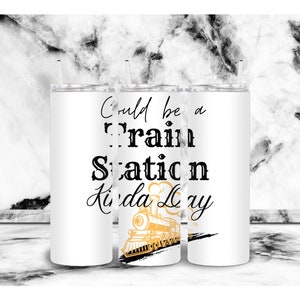 May include: White tumbler with black text that reads "Could be a train station kinda day" with a gold train illustration.