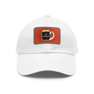 May include: White baseball cap with a red patch featuring a black mug with a yellow foam top and the text "Vitamin G".