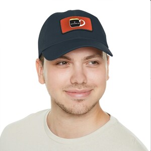 May include: A navy blue baseball cap with an orange patch featuring a black coffee mug with the text "Vitamin C" in white.