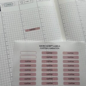 Puede incluir: Una hoja de etiquetas rectangulares de micro script en un tono rosa apagado, con el texto CUSTOM | CARNATION y CORAL AND PAPER. Las etiquetas est&aacute;n dispuestas en columnas, con una etiqueta aplicada en una p&aacute;gina de agenda con cuadr&iacute;cula.