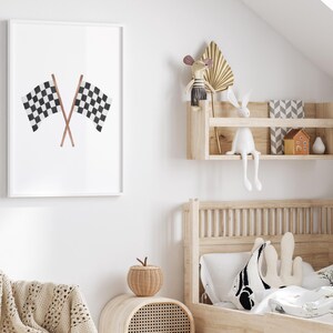 May include: A framed print featuring two crossed checkered racing flags in black and white. The flags are set against a white background, creating a minimalist design. The artwork is displayed in a bright, airy room, suggesting a children's bedroom theme.