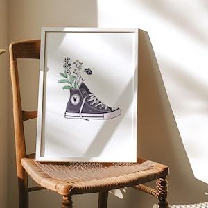 May include: A framed print of a grey canvas shoe with a white heart on the side. Flowers and a small butterfly are growing out of the shoe.