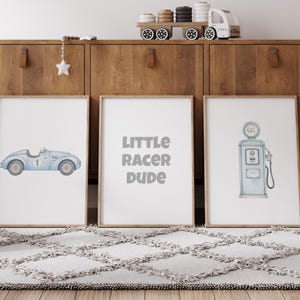 May include: Three framed prints with a racing theme. One features a light blue race car, another reads "LITTLE RACER DUDE," and the third depicts a vintage gas pump, all in soft watercolor style. The prints are displayed on a rug.