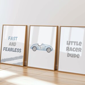 May include: Three framed art prints with a racing theme. One print reads "FAST AND FEARLESS" with tire track accents. The second print features a blue vintage race car. The third print says "LITTLE RACER DUDE". All prints have a white background.