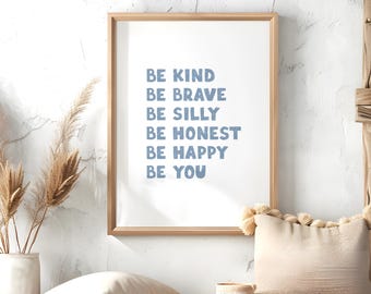 Puede incluir: Un cartel enmarcado con las palabras "BE KIND, BE BRAVE, BE SILLY, BE HONEST, BE HAPPY, BE YOU" en letras azules. El cartel está en un marco de madera clara y se muestra en una pared blanca. Elementos decorativos: un jarrón con plantas secas y un cojín beige.