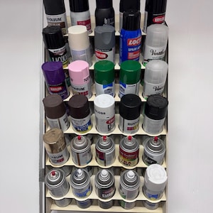 以下が含まれることがあります： スプレー塗料缶が複数列に並んだ木製棚。缶は、Rust-Oleum、Krylon、Valsparなど、さまざまな色とブランドがあります。